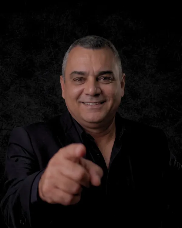 Ricardo Zanga, Gestor de Performance Digital, apontando para a câmera com terno escuro em fundo preto